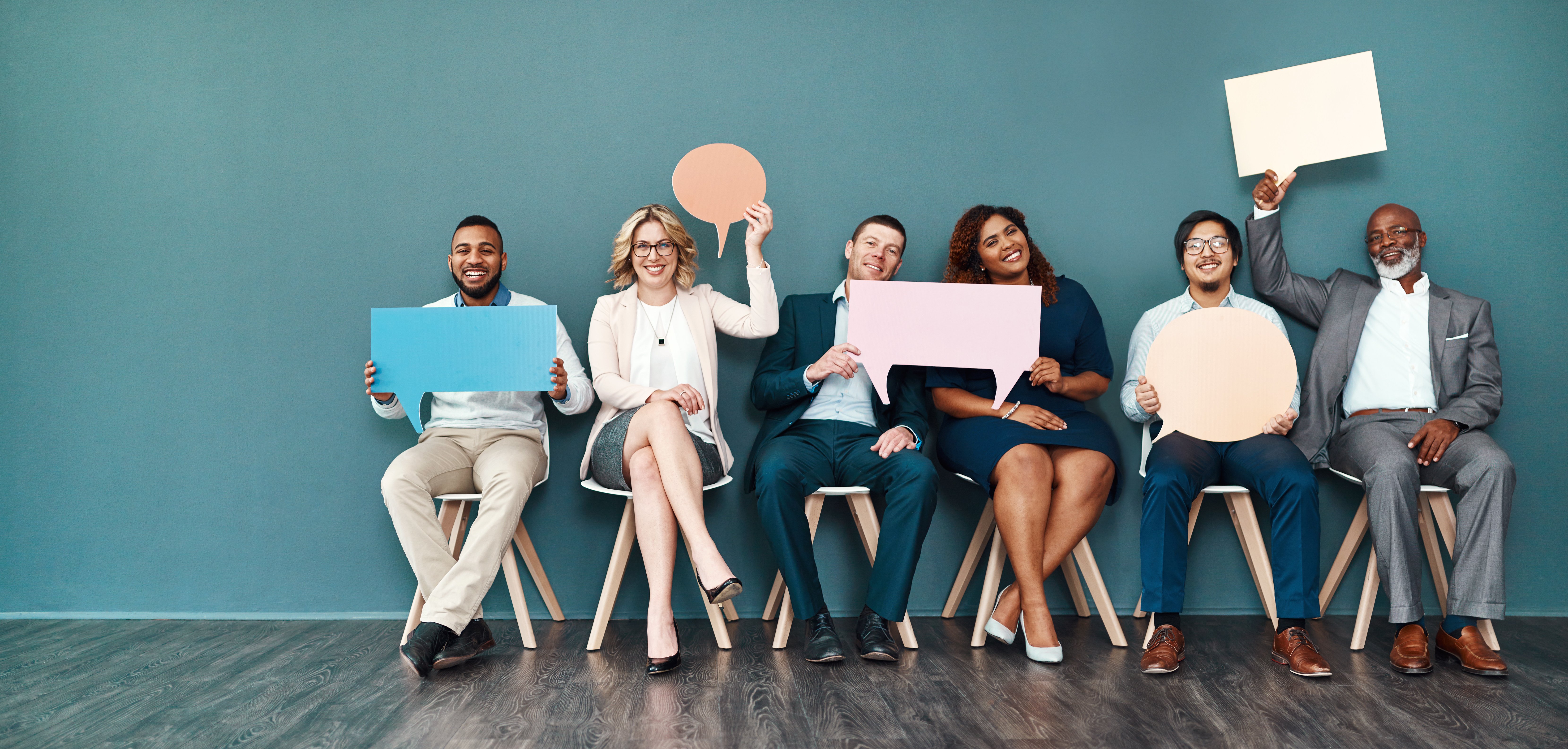 6 job candidates sitting in a row of chairs smiling