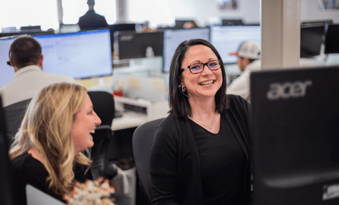 Two women laughing at a computer desk 